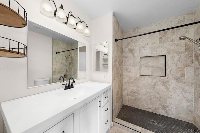 bathroom with a tile shower, vanity, and toilet
