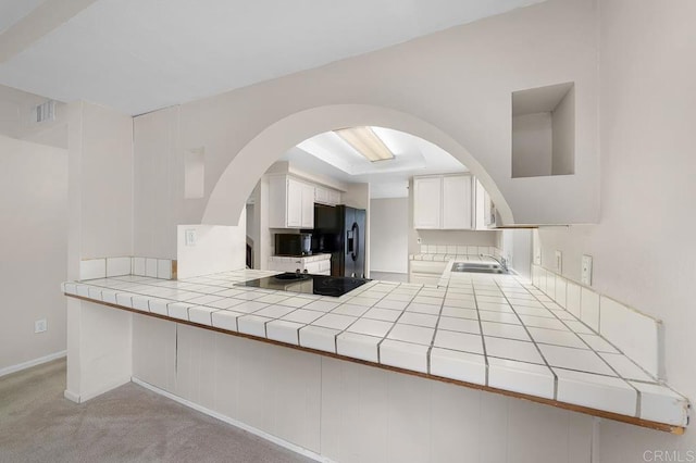 kitchen featuring black appliances, tile counters, a sink, and arched walkways
