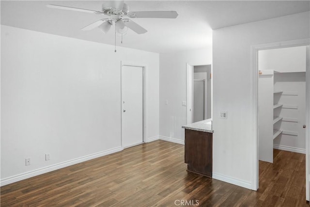 unfurnished bedroom with a spacious closet, dark wood finished floors, a closet, and baseboards