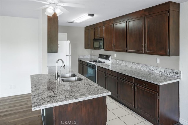 kitchen featuring gas stove, black microwave, a sink, a ceiling fan, and dark brown cabinetry