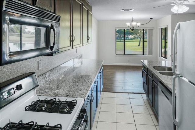 kitchen with white appliances, a chandelier, dark brown cabinetry, a sink, and light stone counters