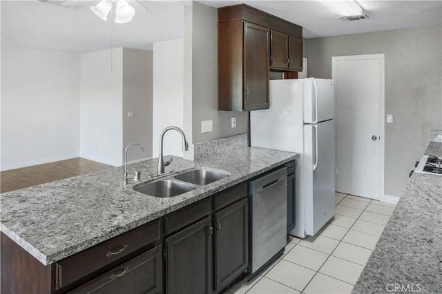 kitchen with a sink, dishwasher, a ceiling fan, dark brown cabinetry, and light stone counters