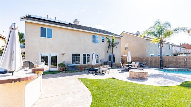 rear view of property with french doors, a patio area, roof mounted solar panels, stucco siding, and a chimney