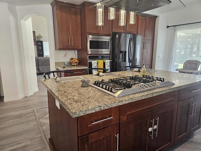 43075 Corte Fresca, Temecula, CA 92592 - kitchen with appliances with stainless steel finishes, arched walkways, light stone counters, exhaust hood, and a center island