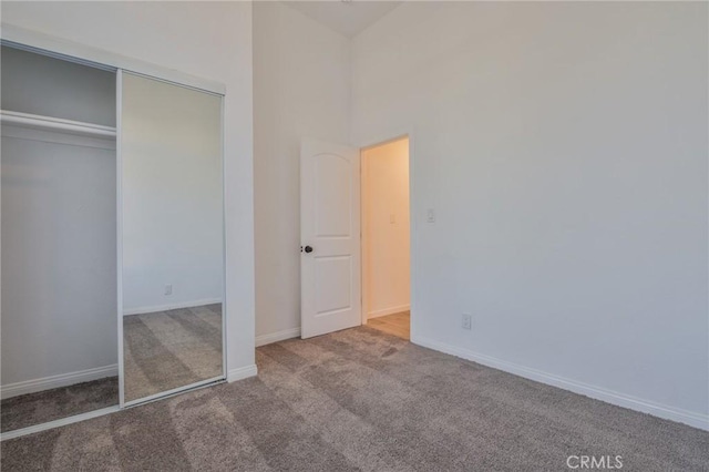 unfurnished bedroom featuring carpet flooring, baseboards, a closet, and a towering ceiling