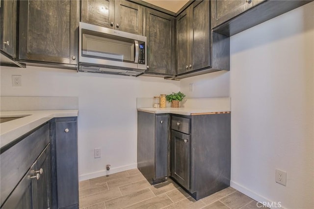 kitchen featuring stainless steel microwave, baseboards, light countertops, and wood finish floors