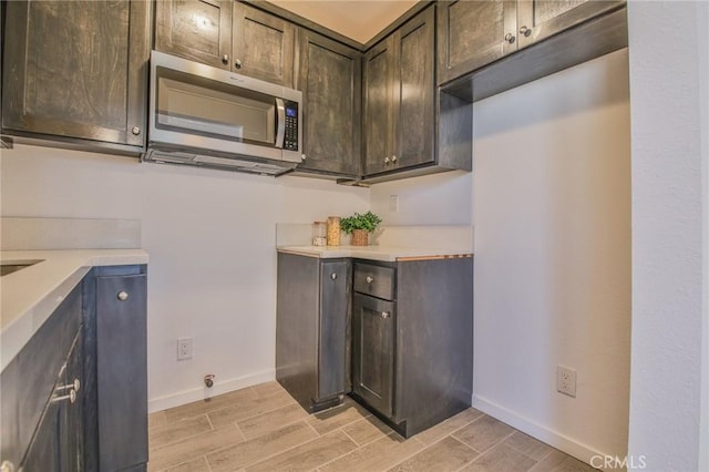 kitchen featuring stainless steel microwave, baseboards, wood tiled floors, and light countertops