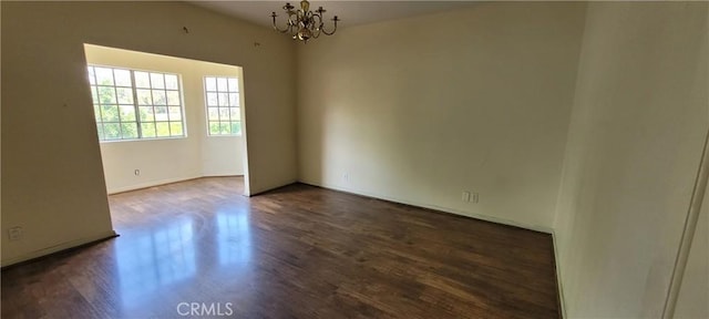 unfurnished room with a chandelier, dark wood finished floors, and baseboards