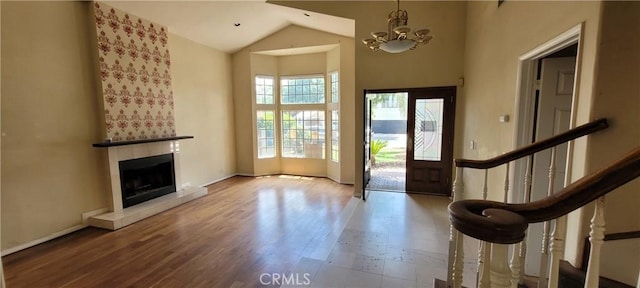 foyer entrance with high vaulted ceiling, a chandelier, a tiled fireplace, wood finished floors, and baseboards