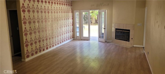 unfurnished living room with wood finished floors, baseboards, and a tiled fireplace