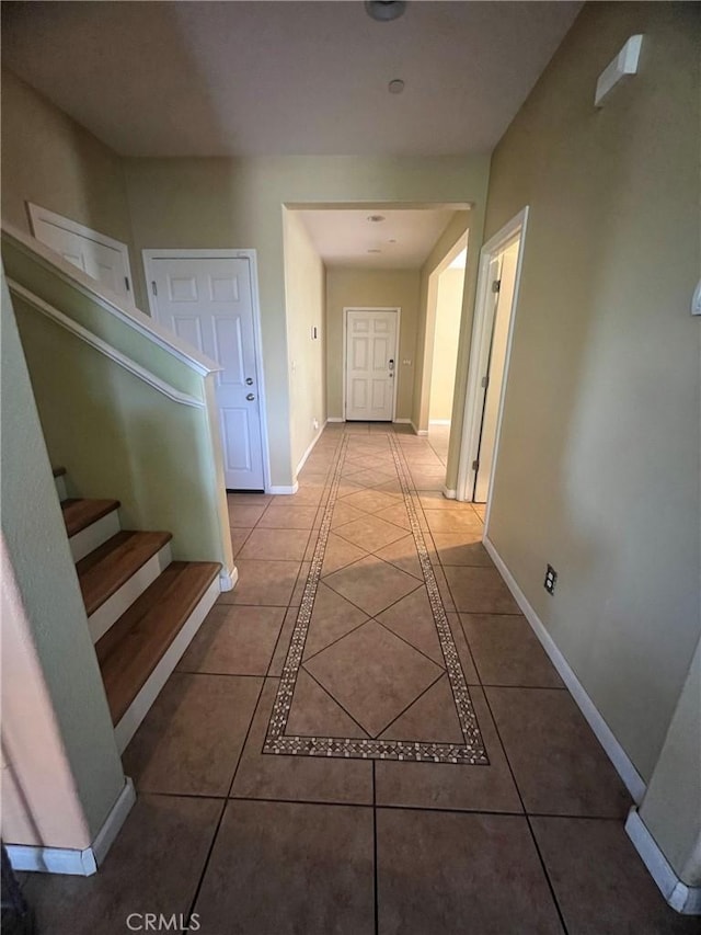 hallway featuring light tile patterned flooring, baseboards, and stairs