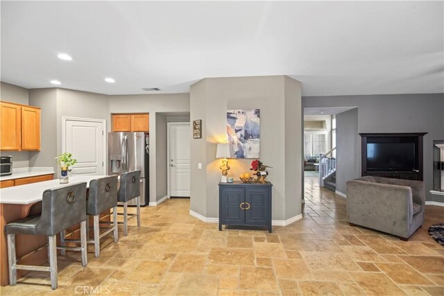 34274 Deergrass Way, Lake Elsinore, CA 92532 - kitchen with stainless steel fridge, light countertops, a kitchen breakfast bar, stone tile flooring, and recessed lighting