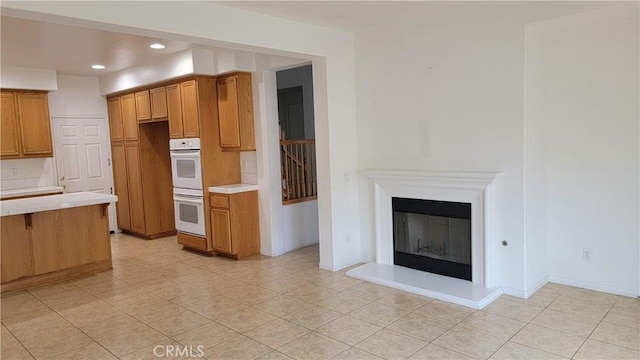 29746 Maxmillian Ave, Murrieta, CA 92563 - kitchen with white double oven, recessed lighting, tile countertops, brown cabinetry, and a glass covered fireplace