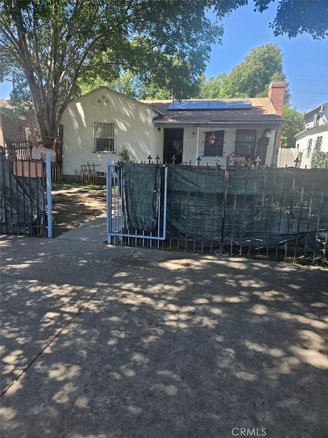151 E 92nd St, Los Angeles, CA 90003 - view of front facade with stucco siding, solar panels, a chimney, and a gate