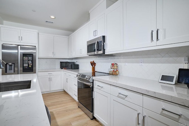 kitchen featuring stainless steel appliances, white cabinetry, decorative backsplash, light stone counters, and recessed lighting