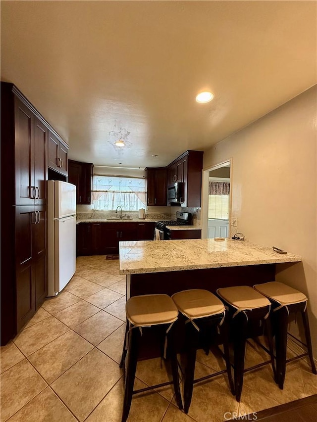 14120 Dillerdale St, La Puente, CA 91746 - kitchen featuring stainless steel appliances, a sink, light stone countertops, dark brown cabinetry, and a breakfast bar