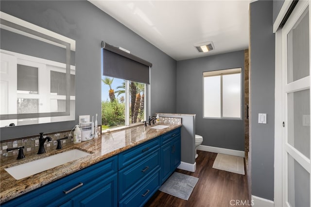 bathroom featuring toilet, wood finished floors, double vanity, and baseboards