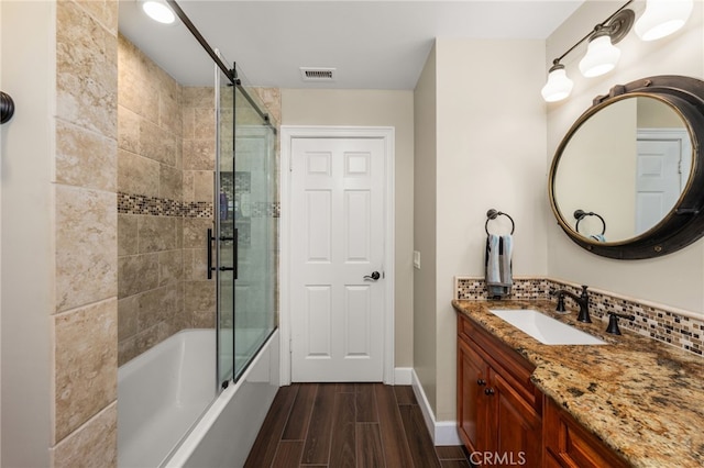 bathroom with wood finished floors, vanity, decorative backsplash, enclosed tub / shower combo, and baseboards