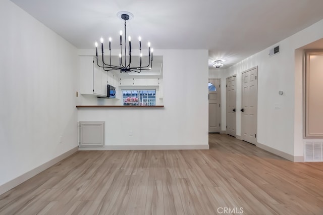 unfurnished living room featuring a chandelier, light wood-type flooring, and baseboards