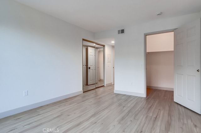 unfurnished bedroom featuring light wood-style flooring, baseboards, a walk in closet, and a closet