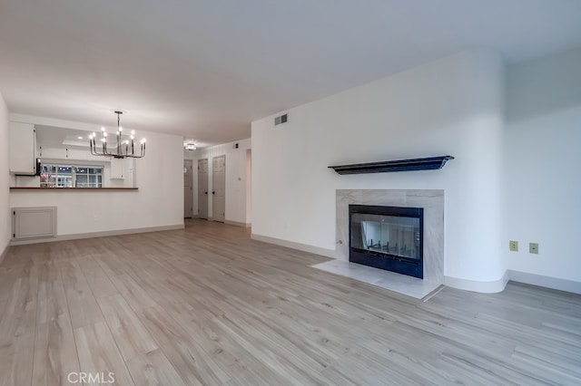 unfurnished living room with a chandelier, a high end fireplace, light wood-type flooring, and baseboards