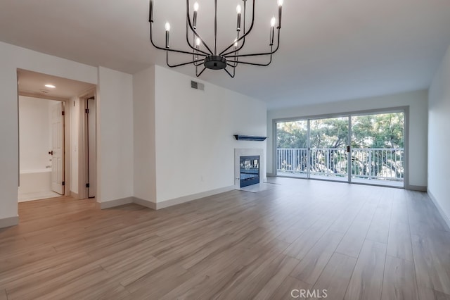 unfurnished living room featuring wood finished floors, a chandelier, baseboards, and a tiled fireplace