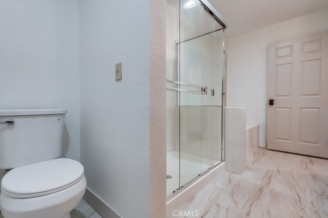 bathroom with a stall shower, toilet, marble finish flooring, and a textured wall