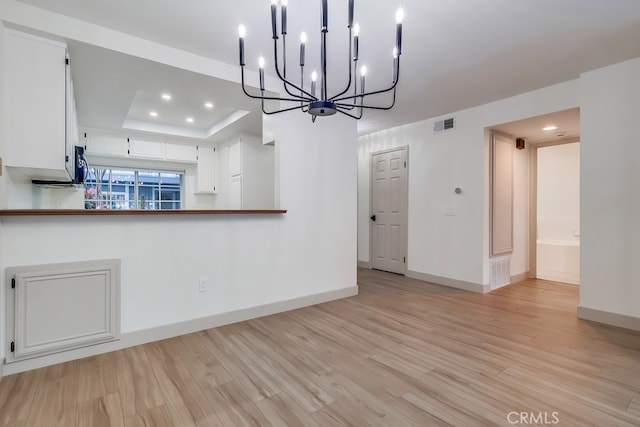 unfurnished dining area with light wood-style floors, baseboards, a chandelier, a tray ceiling, and recessed lighting