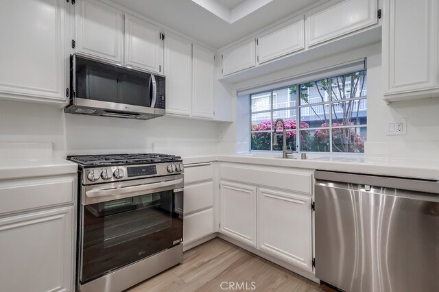 kitchen with appliances with stainless steel finishes, light countertops, white cabinets, light wood finished floors, and a sink
