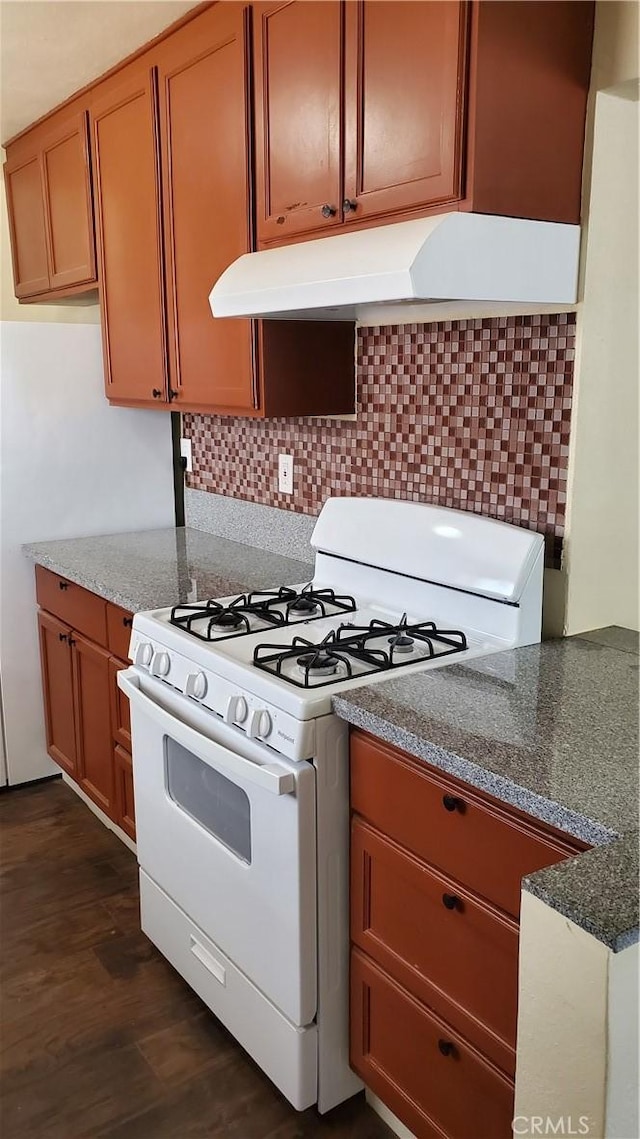 44709 6th St E, Lancaster, CA 93535 - kitchen featuring white gas range oven, under cabinet range hood, backsplash, dark wood-style flooring, and brown cabinetry