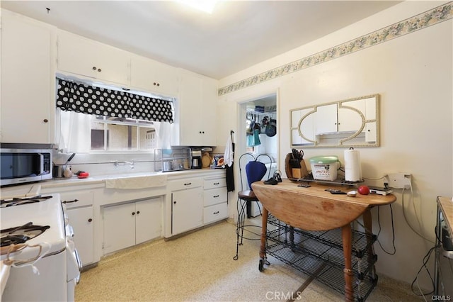 kitchen featuring stainless steel microwave, white gas range oven, light countertops, a sink, and white cabinetry