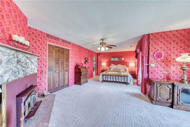 bedroom with wallpapered walls, carpet, a wood stove, a textured ceiling, and a ceiling fan