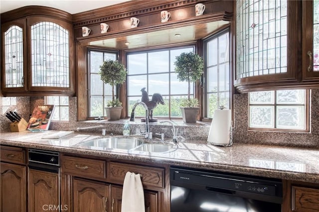 kitchen with dishwasher, a sink, decorative backsplash, glass insert cabinets, and brown cabinetry