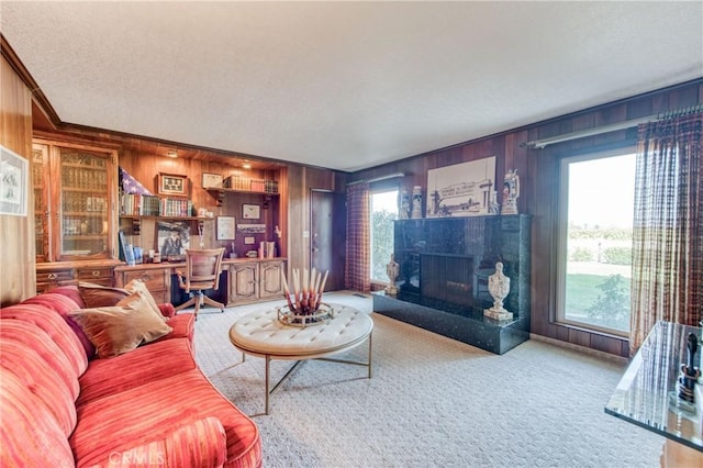 carpeted living area with wooden walls, a textured ceiling, healthy amount of natural light, a high end fireplace, and crown molding