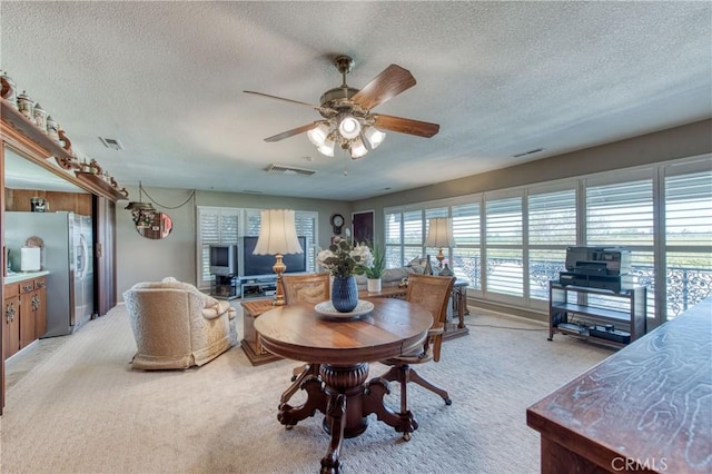 dining room with a textured ceiling, light colored carpet, and ceiling fan