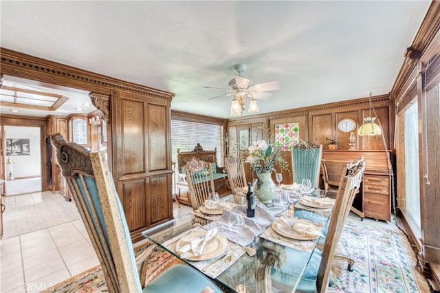 dining space with a ceiling fan, light tile patterned floors, and wood walls