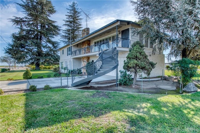 back of property featuring brick siding, a yard, a balcony, and stairs