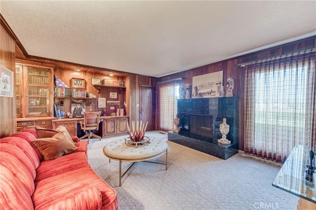 carpeted living area with wooden walls, a fireplace with raised hearth, crown molding, and a textured ceiling
