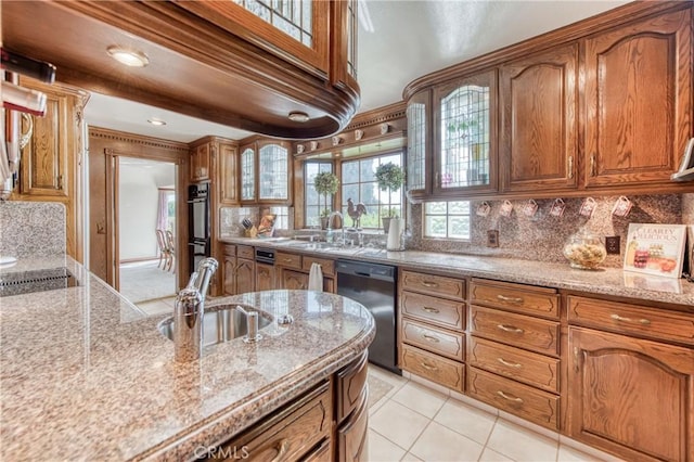 kitchen with black appliances, brown cabinetry, a sink, backsplash, and glass insert cabinets