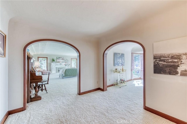 corridor featuring arched walkways, carpet flooring, and baseboards