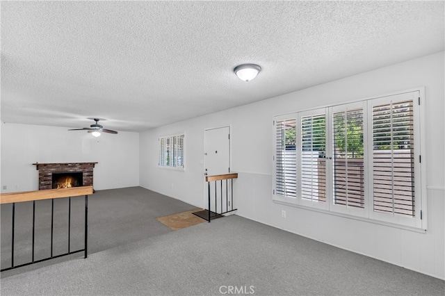unfurnished living room with carpet, a textured ceiling, a ceiling fan, healthy amount of natural light, and a fireplace
