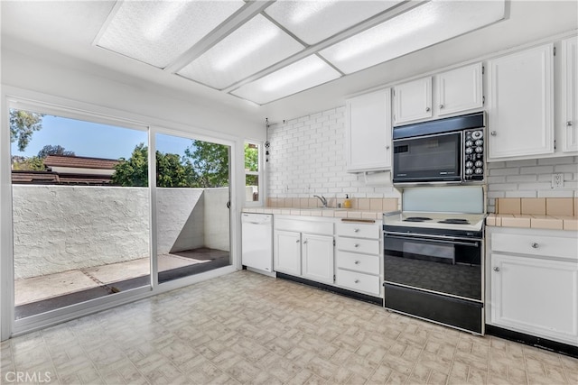 kitchen featuring black microwave, electric stove, tile counters, dishwasher, and white cabinets