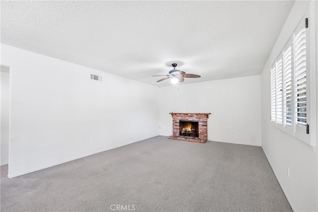 unfurnished living room with a ceiling fan, carpet, a brick fireplace, and a textured ceiling