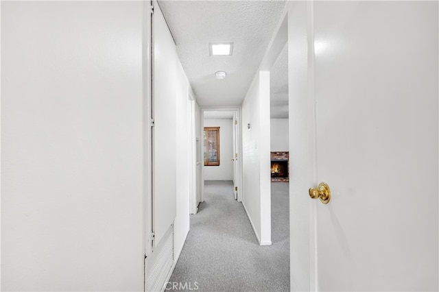 hall with a textured ceiling, light colored carpet, and baseboards