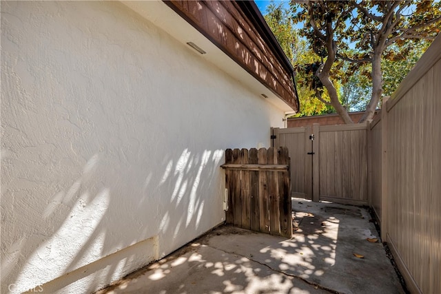 view of side of property featuring stucco siding, a gate, fence, and a patio area