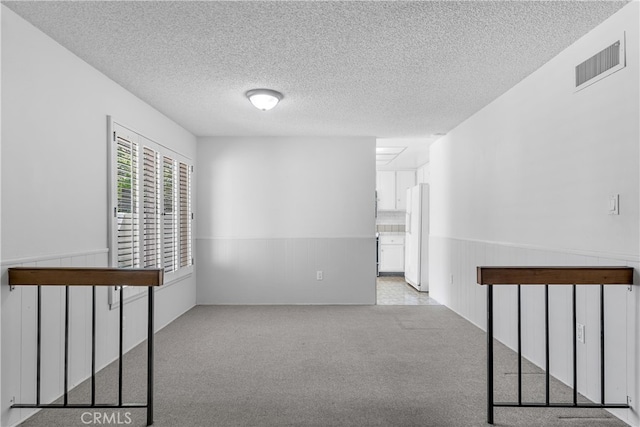 empty room with a wainscoted wall, a textured ceiling, and carpet flooring