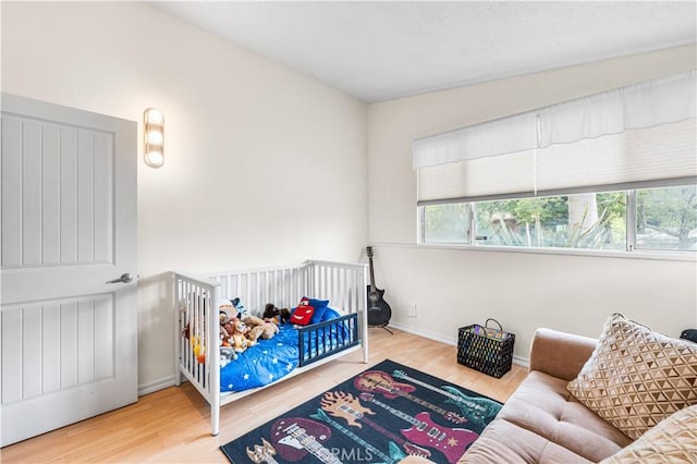 bedroom with wood finished floors, baseboards, and a nursery area
