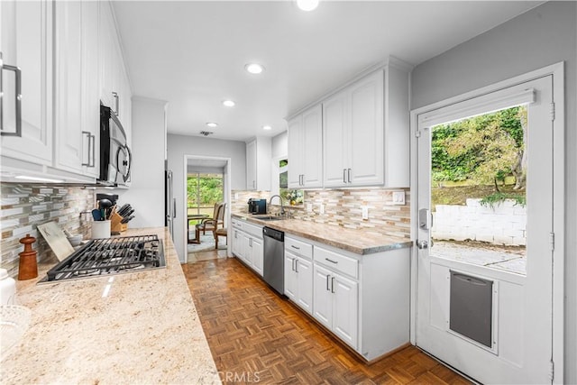 kitchen featuring stainless steel appliances, a sink, decorative backsplash, white cabinets, and plenty of natural light