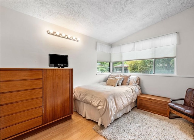 bedroom featuring vaulted ceiling, a textured ceiling, and light wood-type flooring