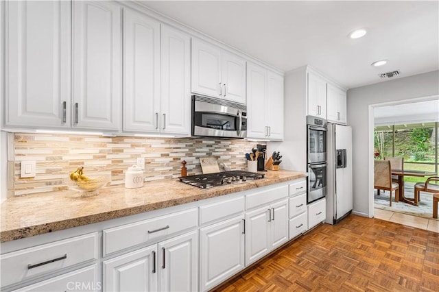 kitchen with appliances with stainless steel finishes, white cabinets, recessed lighting, backsplash, and light stone countertops